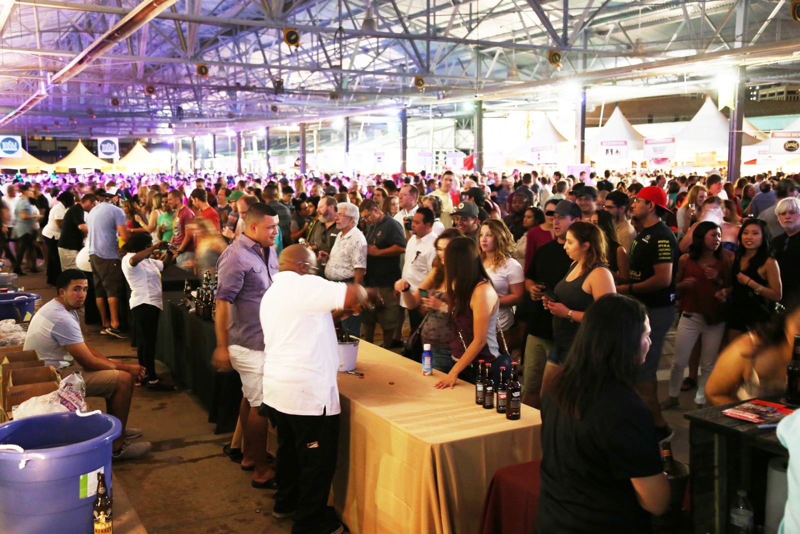 Dallas Arts BrewFest — hundreds of guests fill The Shed at Dallas Farmers Market under purple festival lighting with vendor tables throughout