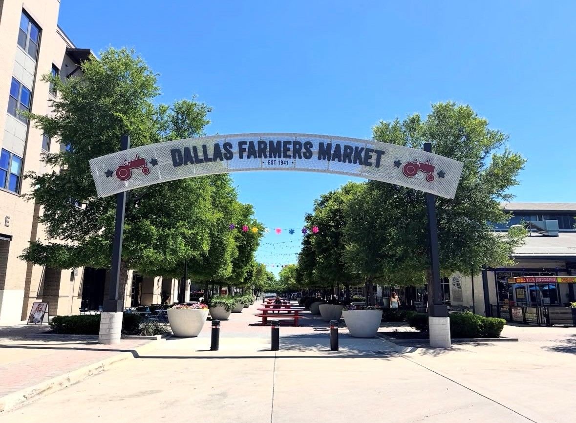 The Pearl Plaza arch sign — Dallas Farmers Market Est. 1941 — framing a tree-lined walkway with string lights and outdoor event space