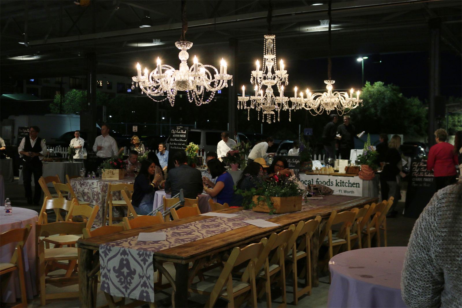 Crystal chandeliers and candlelit farm tables inside The Shed at Dallas Farmers Market during an evening gala